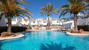 Una piscina con palmeras, un edificio blanco con balcones y un flotador.