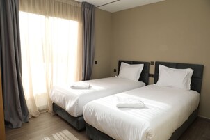 A hotel room with two beds, a large window with curtains, and a wooden floor.