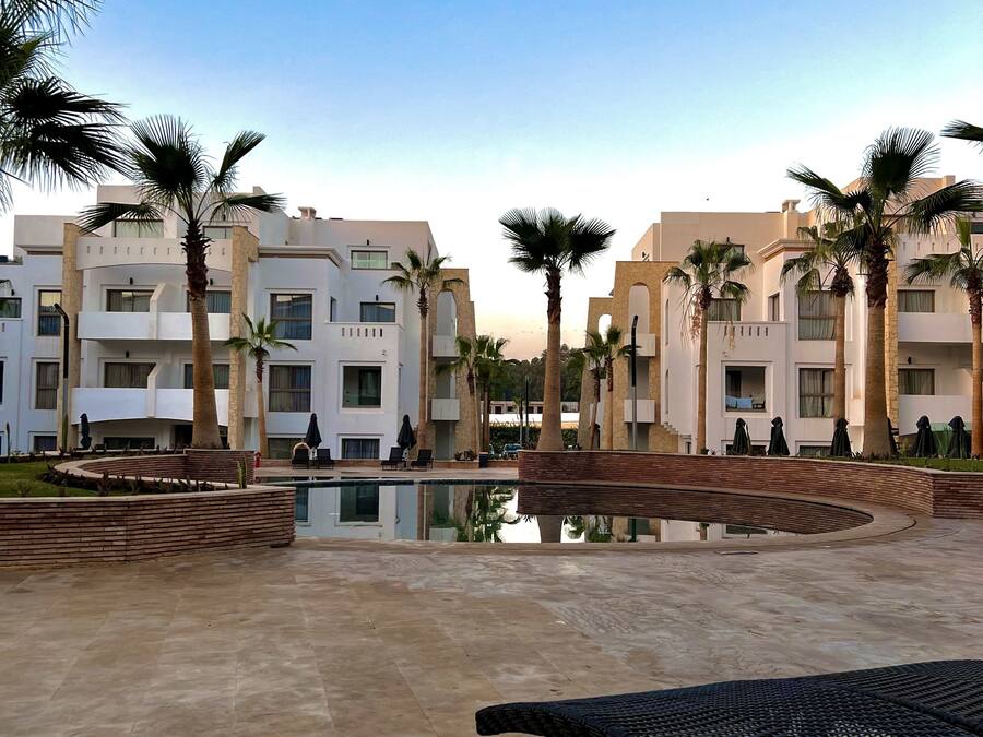 A modern hotel courtyard with a central pool, palm trees, and a lounge area.