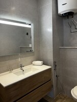 Un baño moderno con un espejo grande, un lavabo blanco y una ducha.