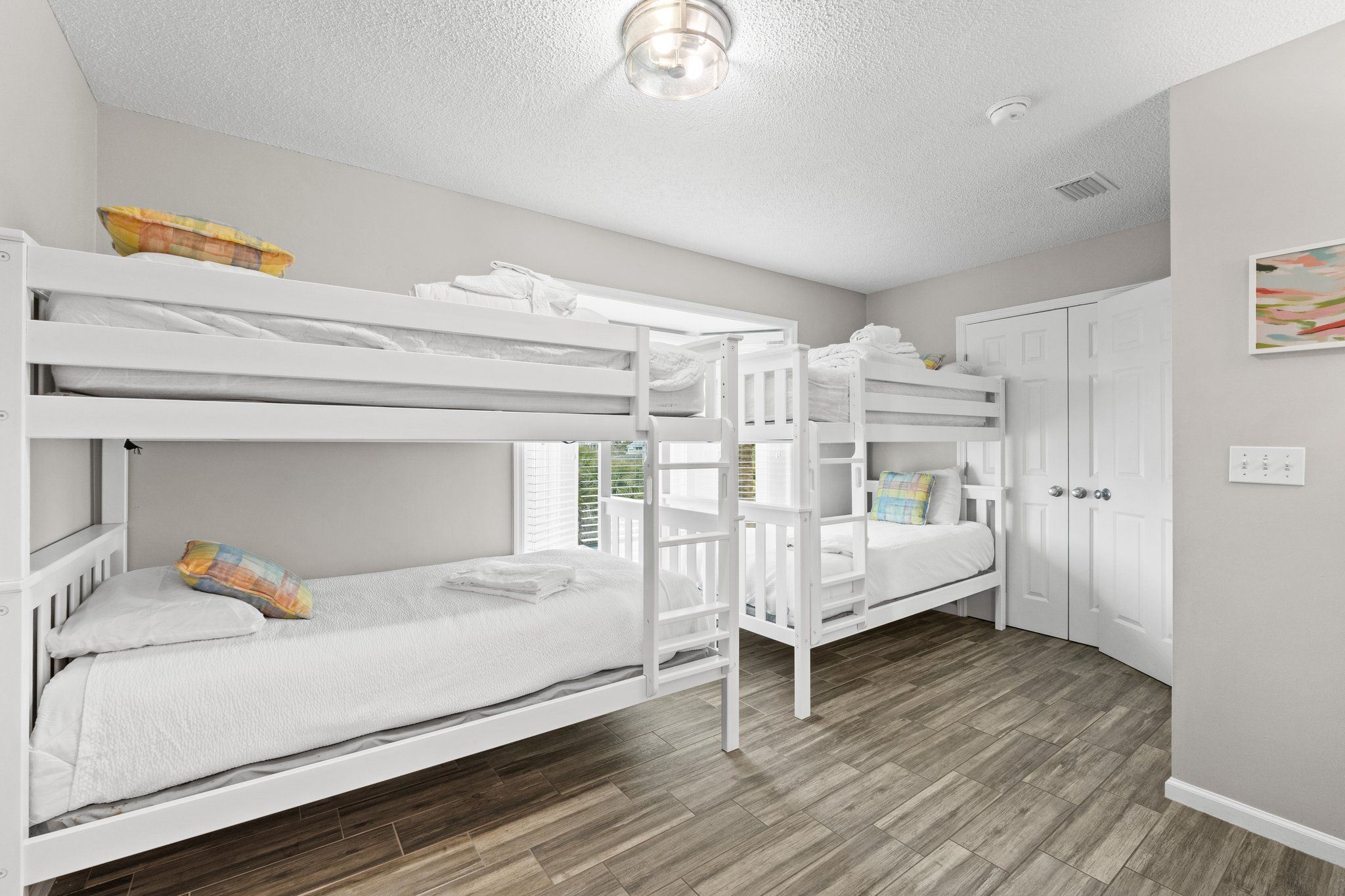A bunk bed room with white bedding, a wooden floor, and a white wardrobe.
