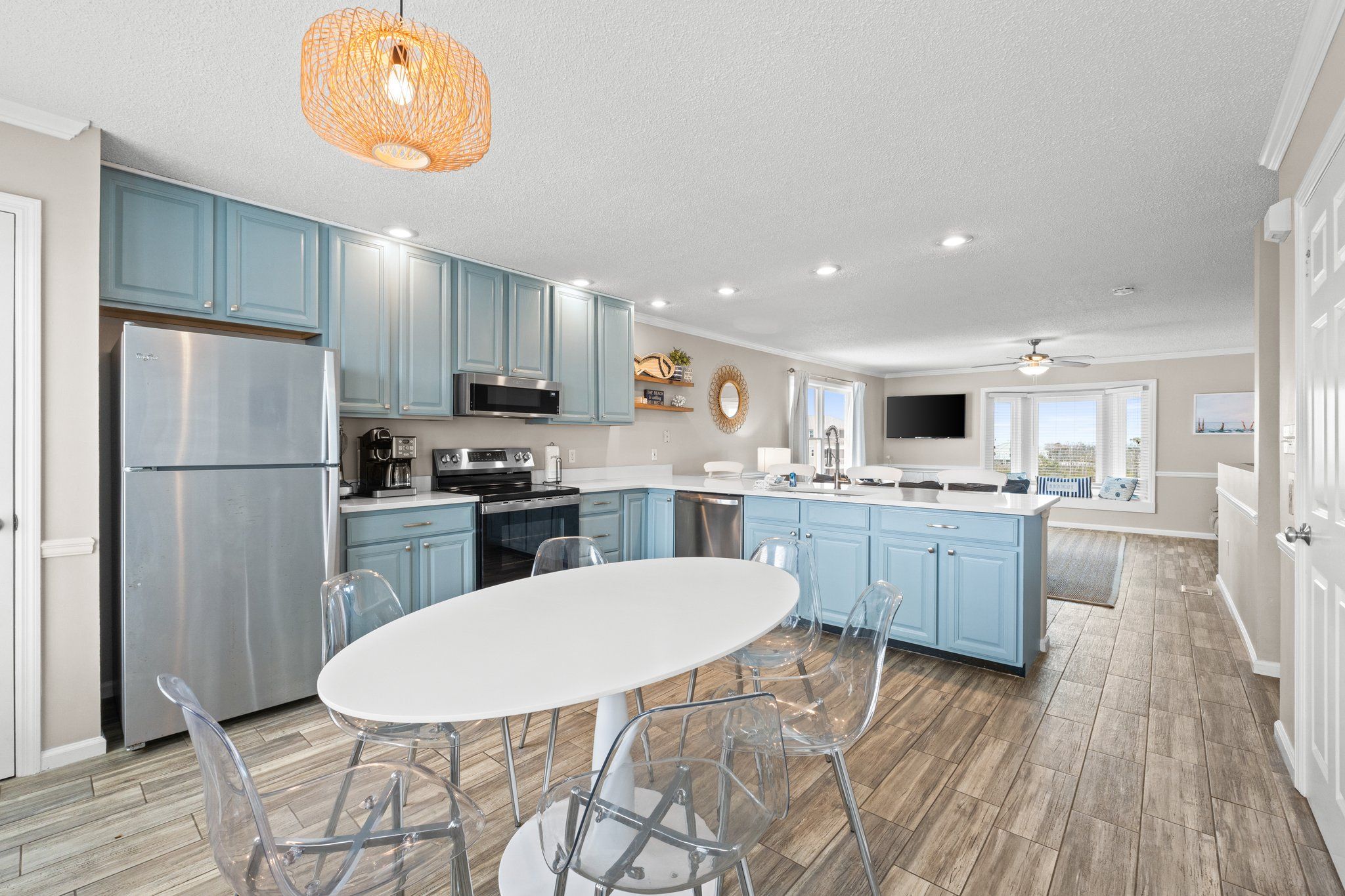 A modern kitchen with light blue cabinets, a stainless steel refrigerator, and a white dining table with clear chairs.
