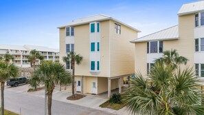 A multi-story hotel with a flat roof, beige exterior, and white trim. There are palm trees in front, and a vehicle parked on the street.