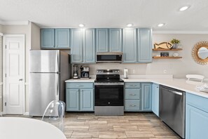 A modern kitchen with light blue cabinets, stainless steel appliances, and a wooden floor.