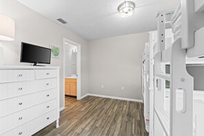 A child's playroom with a TV, white dresser, bunk beds, and a wooden floor.