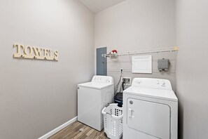A laundry room with two white washers and dryers, a wall-mounted towel rack, and a laundry basket on the floor.