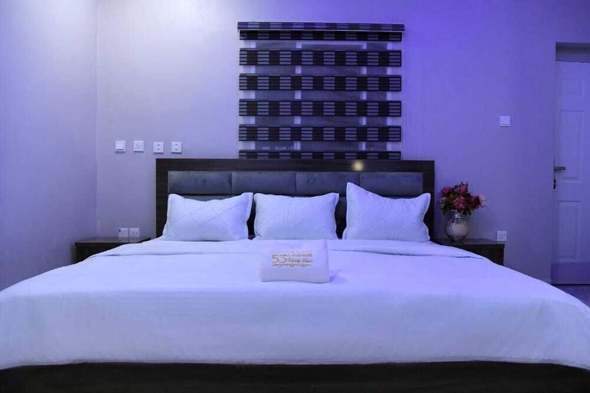 A neatly made bed with white linens and pillows, a decorative wall panel, and a vase with flowers on a nightstand.