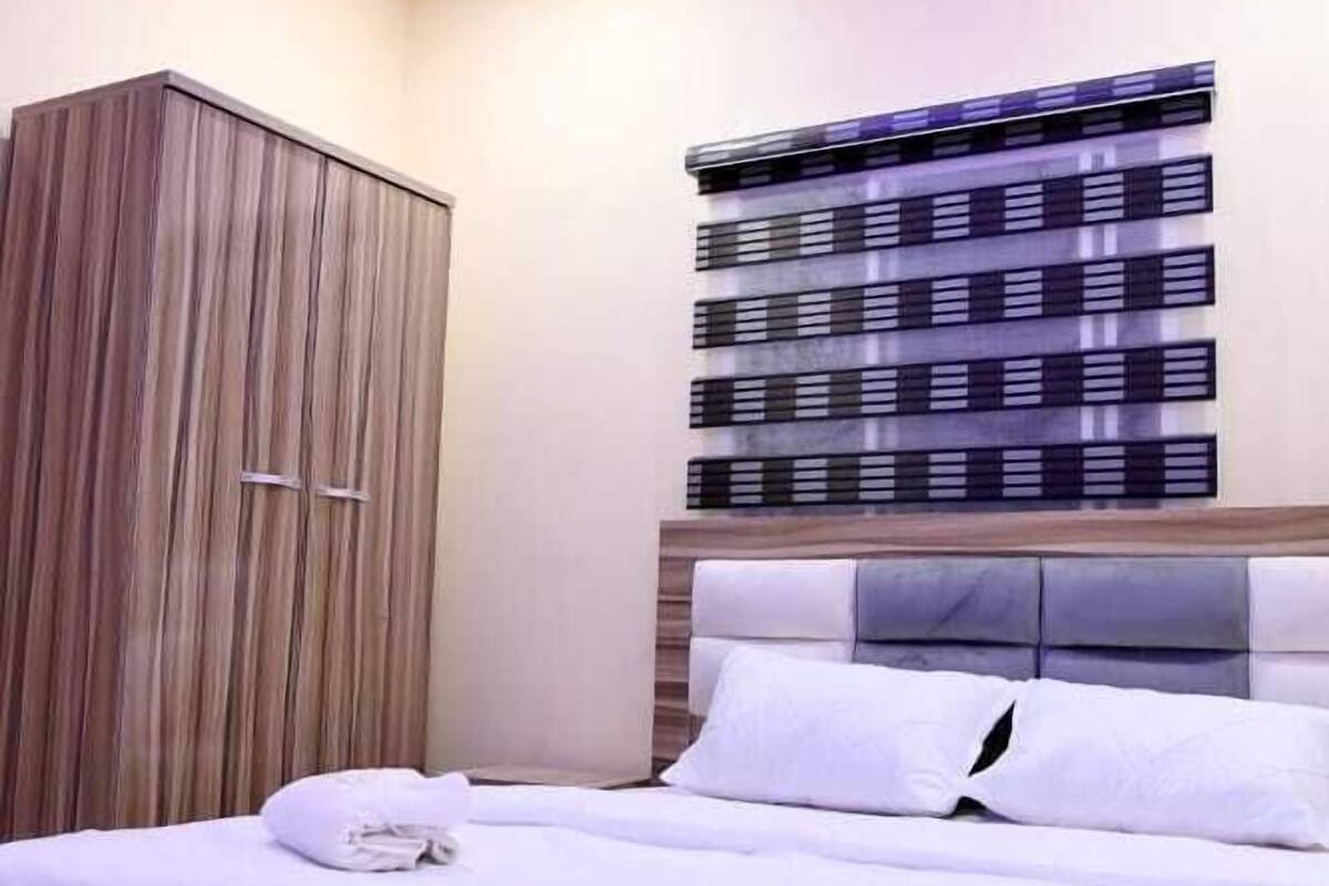 A neatly arranged bedroom with a bed, a wardrobe, and a decorative wall panel.