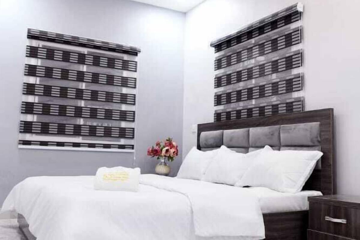 A modern bedroom with a bed, bedside tables, an air conditioning unit, and a decorative wall panel.