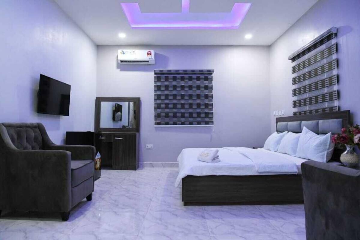 A modern bedroom with a bed, a TV, a dresser, and a wall-mounted air conditioner.
