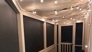 A room with large windows, a wooden floor, and string lights. - Relaxing 2 BR cottage, walking distance to beach (Hilton Head Island)