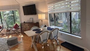 A dining area with a wooden table, wicker chairs, and a TV mounted on the wall. - Relaxing 2 BR cottage, walking distance to beach (Hilton Head Island)
