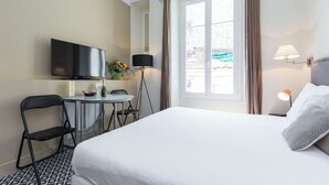 Una camera d'albergo con un letto, una televisione, un tavolino con sedie, una lampada e una finestra con tende.