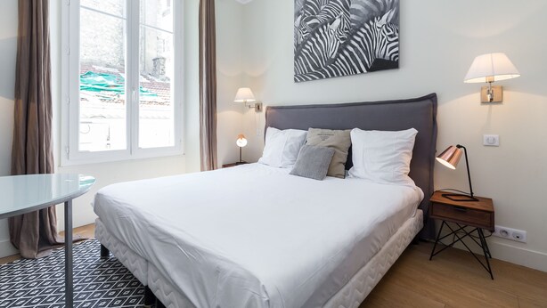 Un letto rifatto con lenzuola bianche, una lampada da comodino moderna e un'opera d'arte a tema zebra sulla parete.