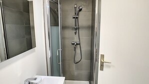 Een moderne badkamer met een douchecabine van glas, een witte wastafel en een spiegel.