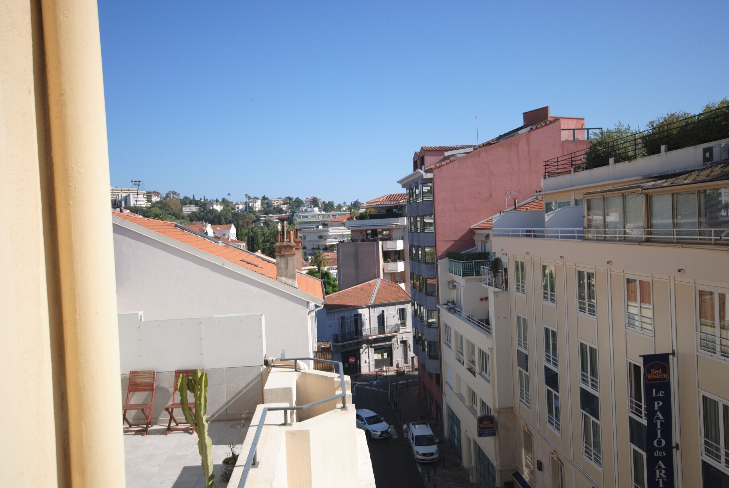 A narrow street with buildings, a clear sky, and a sign for 'Le Patio des Artistes.'