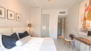 A bedroom with a large bed, a desk, and a chair, a door leading to another room, and framed pictures on the wall. - Cosy studio in Cannes (Cannes)