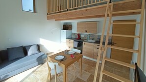 Een compacte leefruimte met een stapelbed, kitchenette en een eethoek met een tafel en stoelen.