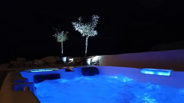Een bubbelbad met blauw licht, omringd door rotsen en twee verlichte bomen.