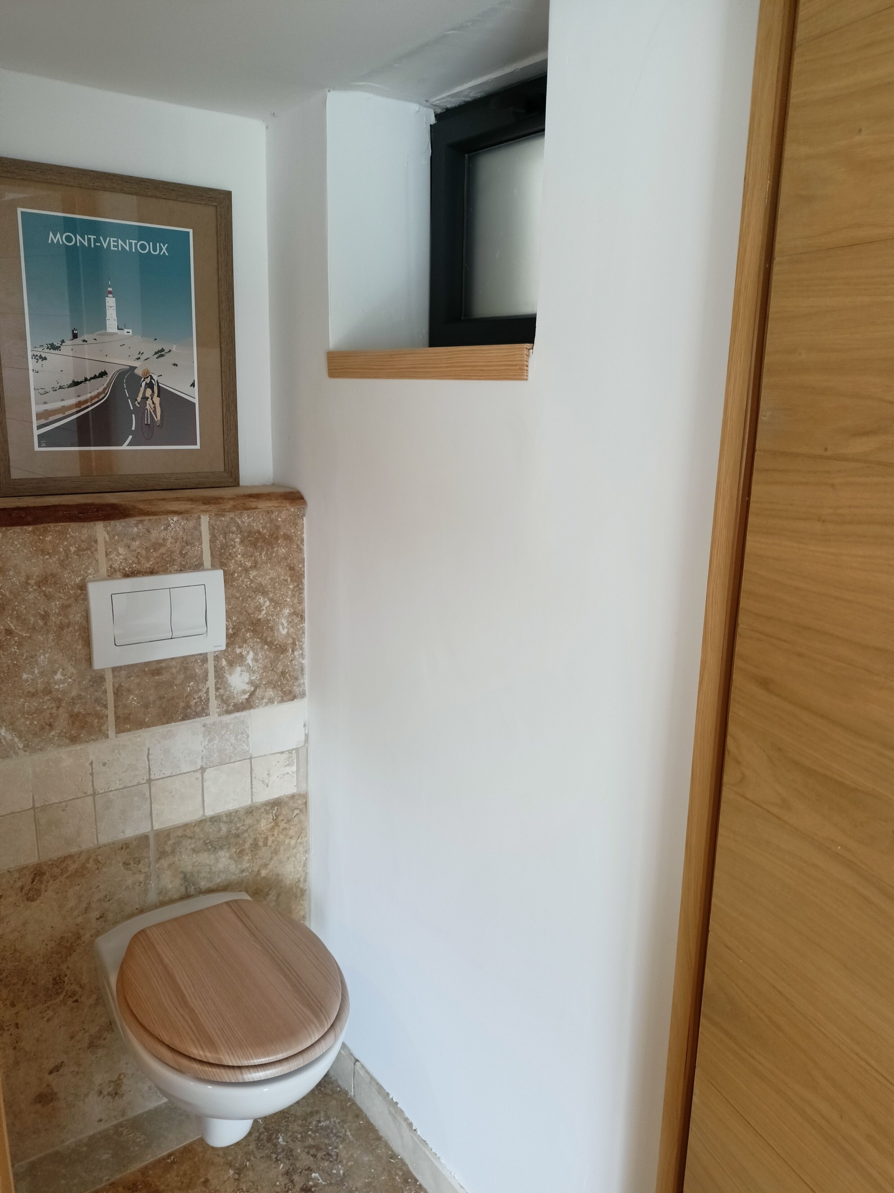 Ein kleines Badezimmer mit einer Holzwc, einem gerahmten Bild an der Wand und einem kleinen Regal darüber.