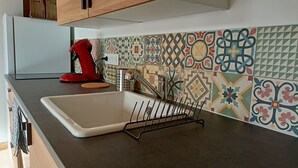 Een keuken met een witte spoelbak, een rode waterkoker en een kleurrijke tegelachtergrond.