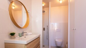 Een moderne badkamer met een houten wastafelmeubel, een ronde spiegel, toilet en douche.