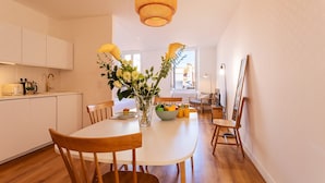 Een moderne keuken met witte kastjes, een eettafel met stoelen, een vaas met bloemen en een fruitschaal.