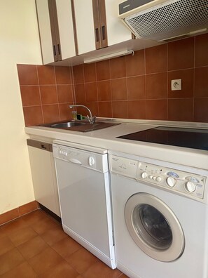 A compact kitchen with a dishwasher, a washing machine, and a sink.
