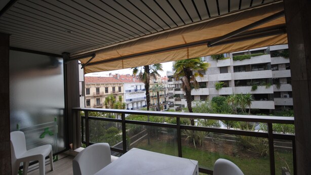 Un balcon avec une table et des chaises, d’où l’on peut admirer un paysage urbain avec des immeubles et des palmiers.