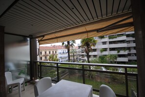 A balcony with a table and chairs, a view of a cityscape with buildings and palm trees.