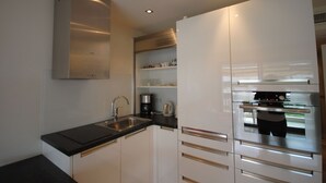 Une cuisine moderne avec des meubles blancs, un plan de travail noir, une hotte en acier inoxydable et des appareils électroménagers intégrés.