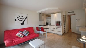 Un salon moderne avec un canapé rouge, une table basse blanche et un coin cuisine doté de placards et d’un plan de travail.