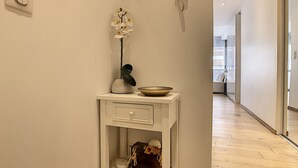 Un pasillo con una consola blanca, un jarrón con flores blancas, un cuenco y un espejo en la pared.