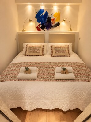 A neatly made bed with a patterned bedspread, two pillows, and two folded towels with tags.