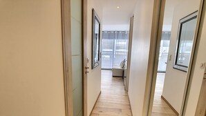 Un pasillo con suelo de madera, una puerta corredera y vistas a una habitación con cama y ventana.