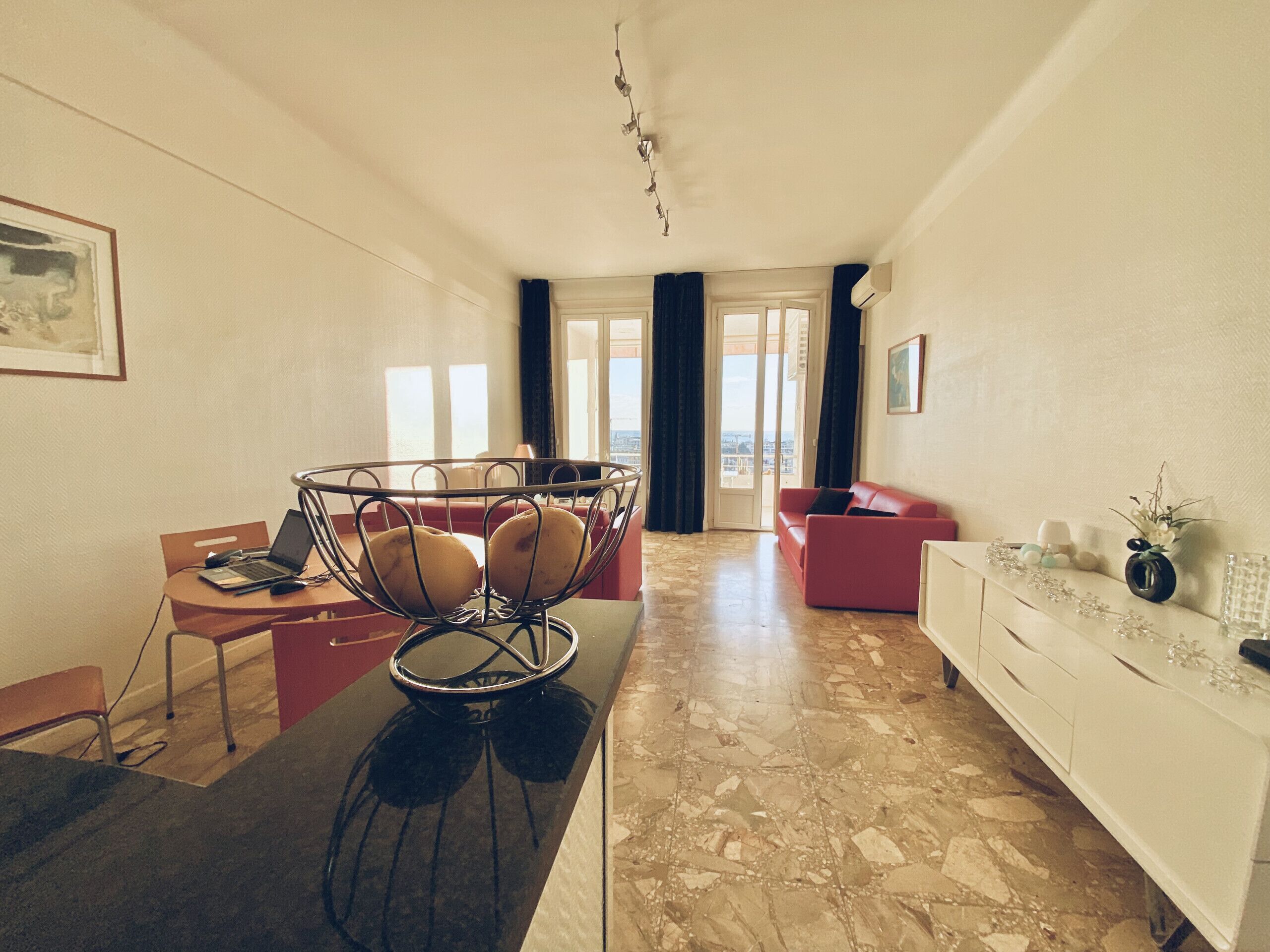 Un salon moderne comprenant un coin repas, un canapé rouge, un meuble blanc et une vue à travers les portes vitrées.
