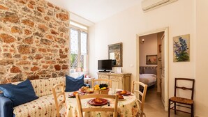 Una habitación acogedora con pared de piedra, una mesa de comedor dispuesta con platos y una cesta de fruta, un sofá con cojines azules y una silla.