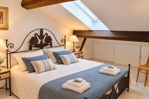 A bedroom with a bed, two bedside tables, a nightstand, a chair, and a skylight.