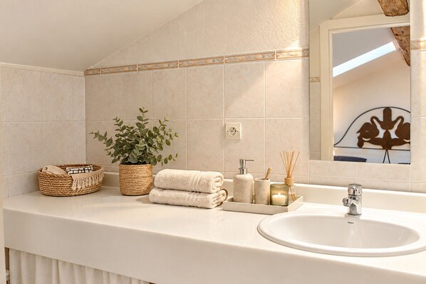 A bathroom with a white sink, a mirror, a potted plant, and a tray with toiletries.