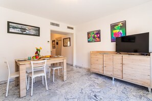 A dining area with a wooden table, white chairs, a TV, and artwork on the walls.