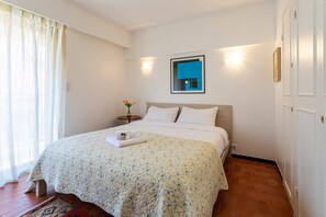 A neatly made bed with a floral bedspread, a bedside table with a vase of flowers, and a wall-mounted mirror.