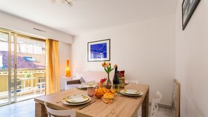A dining area with a wooden table, white chairs, a vase with flowers, and a framed picture on the wall. - Appartement Trois pièces DEB5515 (Cannes)