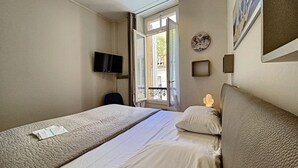 Hotellihuone, jossa on sänky, televisio, ikkuna ja seinäkello.
