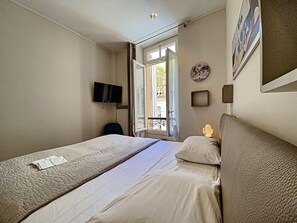 Een hotelkamer met een bed, een televisie, een raam en een wandklok.