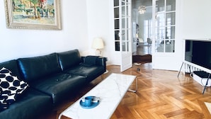 A living room with a black leather sofa, a white coffee table, a painting on the wall, and a TV on a stand. - Riviera Design / Charming apartment 2mn from the beach (Cannes)