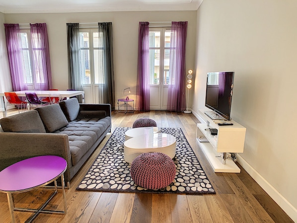 A modern living room with a sofa, coffee table, ottoman, and a flat-screen TV.