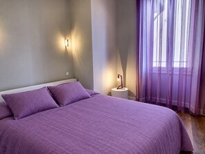 A bedroom with a bed, two bedside lamps, and a window with sheer curtains.