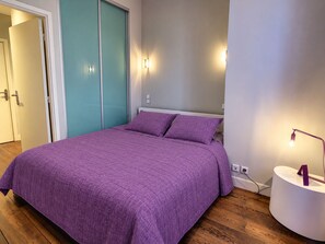 A bedroom with a bed, a nightstand, a wall-mounted lamp, and a door.