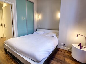 Ein Schlafzimmer mit einem Bett, einem Nachttisch, einer Wandleuchte und einer Tür.