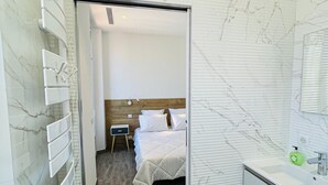 Hotellihuone, jossa on sänky, yöpöytä, kylpyhuone, jossa on pesuallas ja peili, sekä patteri.